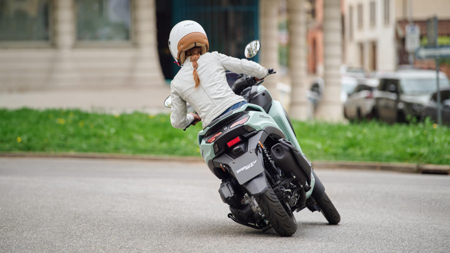 Una Yamaha Tricity 125, vista desde atrás, dobla en una esquina, manejada por una mujer 