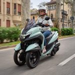 Por qué la Yamaha Tricity 125 es una opción urbana lógica Una mujer joven conduce una Yamaha Tricity 125 verde en un sector urbano con edificios históricos