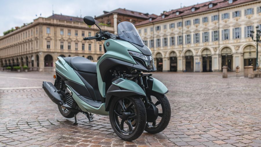 Una Yamaha Tricity 125 2025 de color verde dispuesta para una foto sobre el empedrado de una lugar histórico de una ciudad europea