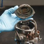 Carburador sucio en la moto: síntomas, causas y soluciones Una mano enguantada abre la tapa de un carburador de moto sucio