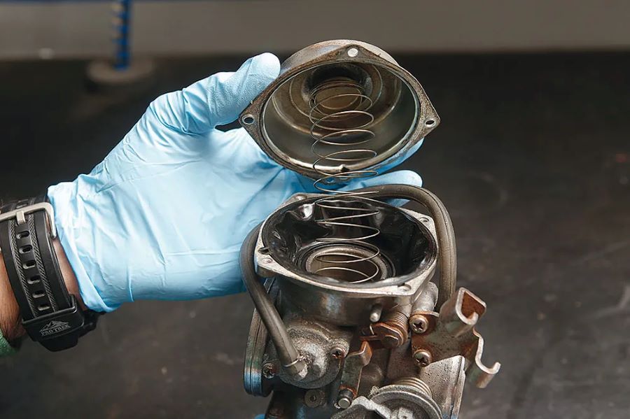 Carburador sucio moto 1 Una mano enguantada abre la tapa de un carburador de moto sucio