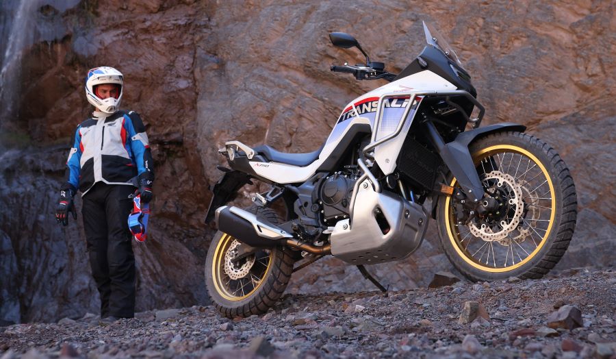 Un usuario, parado y con casco puesto, observa a su Honda XL750 Transalp en un escenario montañoso
