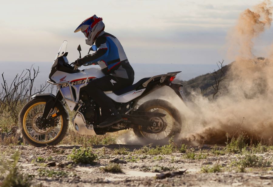 Un piloto sobre una Honda Transalp blanca acelera en un terreno polvoriento