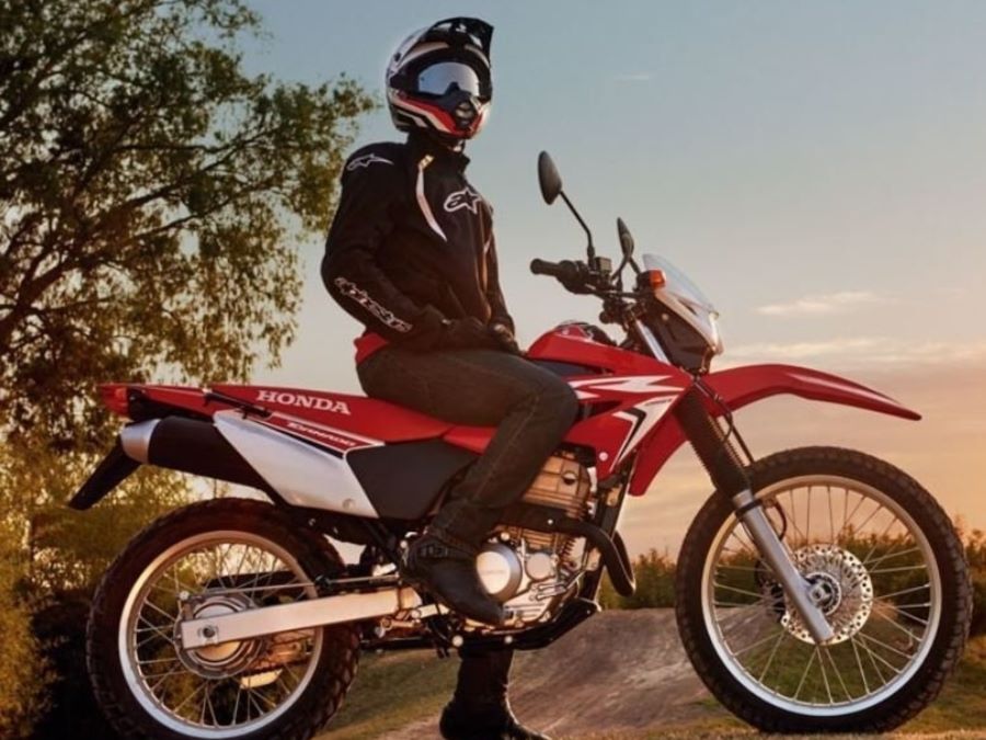 Un piloto. sentado sobre su Honda CB150 Tornado roja. mira hacia el horizonte