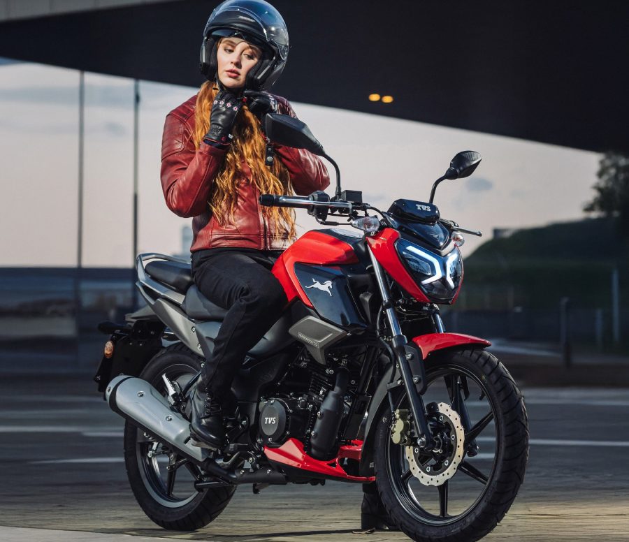 Una joven conductora se ajusta el casco sobre una moto naked TVS roja