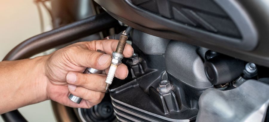 Un mecánico muestra una bujía de moto sucia recién extraída