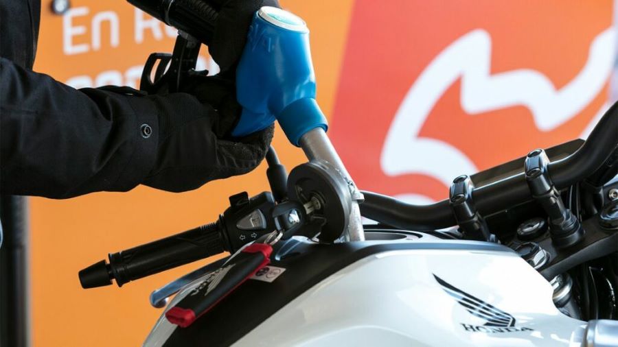 Una manguera de surtidor carga combustible en una moto blanca