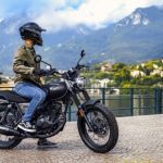 Un piloto joven está sentado sobre su Keeway X-Light 1125 negra observando el lago y las montañas