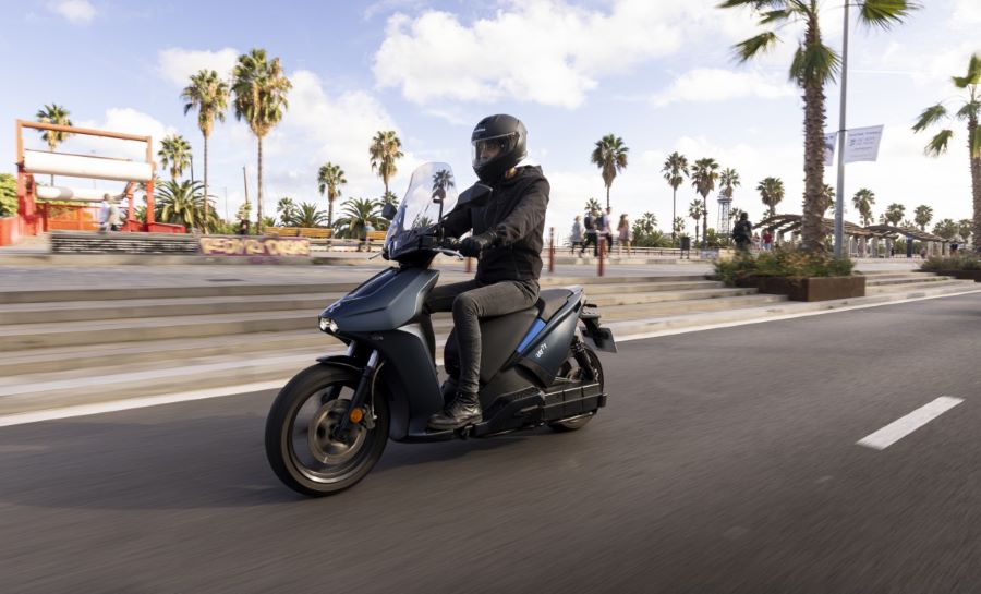 Un scooter eléctrico RAY 7.7 se desplaza por una ruta asfáltica con palmeras a sus costados