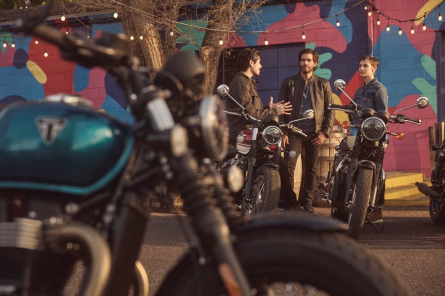 Vista parcial de una Triumph Bonneville azul en primer plano con usuarios y más motos de la gama de fondo