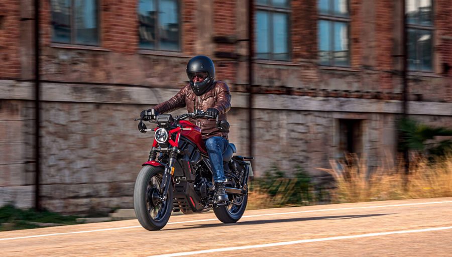 Un usuario se desplaza por una zona de la ciudad con edificios en ruinas con una Zontes 125C roja