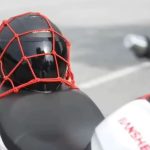 Cómo llevar un casco extra en la moto: práctico y seguro Un casco negro guardado en una red protectora roja sobre el asiento de una moto