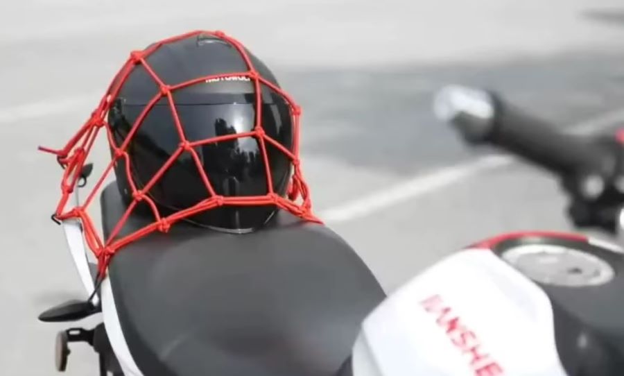 red para casco Un casco negro guardado en una red protectora roja sobre el asiento de una moto
