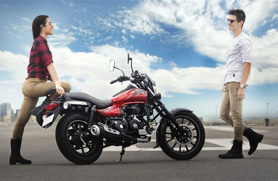 Una mujaer apoya su rodilla sobre una moto Bajaj Avenger 160 y espera a un hombre que se acerca