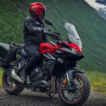 Un usuario de una moto Honda CB1000GT roja se detuvo en una carretra de grava para observar el paisaje montañoso y verde