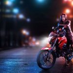 Una mujer joven mira a la cámara sentada sobre una moto Honda CB125F roja e un contexto de calle oscura