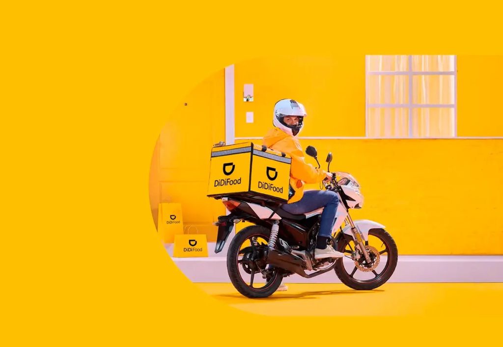 Un conductor de moto de la app Didi Food gira hacia la cámara y sonríe