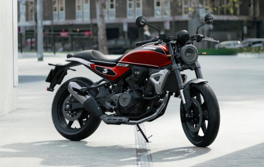 Vista de una Morini 31/2 Sport 2026 roja reposando sobre su pata y con la ciudad de fondo