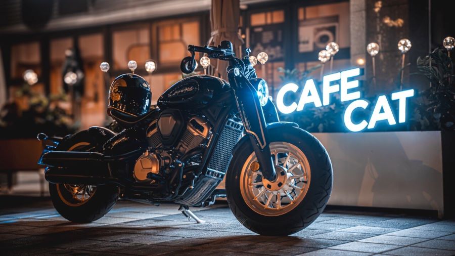 Motor V2 y estilo radical: así es la Benda Napoleon Bob 500 Una Beda Napoleu Bob 500 V2 negra estacionada frente a una vidriera de un café