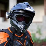 Un motociclista, con casco negro y cámara de acción lateral, mira hacia la lente del fotógrafo