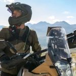 Un motociclista mira hacia un costado sobre su moto, con un dispositivo Garmin inReach Mini 3 Plus colocado sobre la correa de la mochila