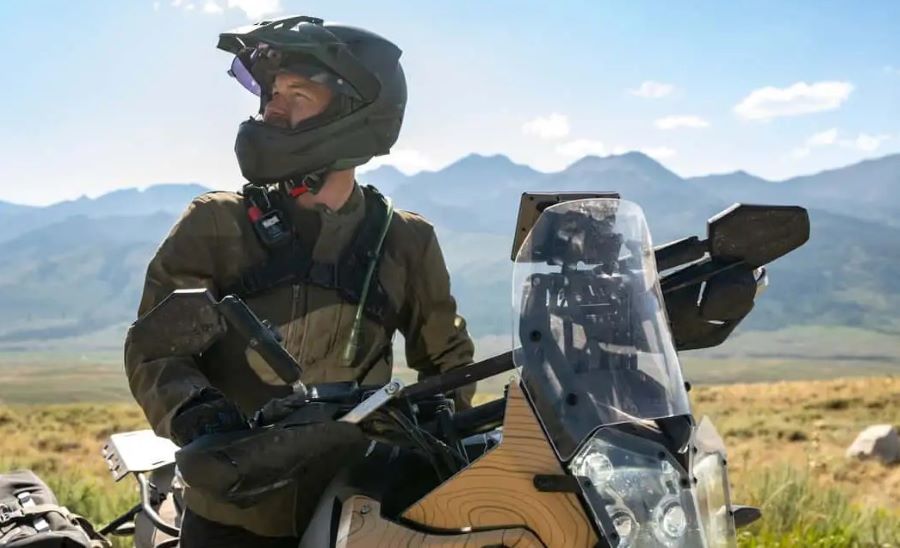 Un motociclista mira hacia un costado sobre su moto, con un dispositivo Garmin inReach Mini 3 Plus colocado sobre la correa de la mochila