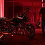 En un ambiente con poca luminosidad, un piloto, casco en mano, se acerca a su Harley-Davidson X440 T negra