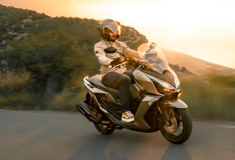 Un scooter Kymco Downtown gris metalizado transita por una ruta