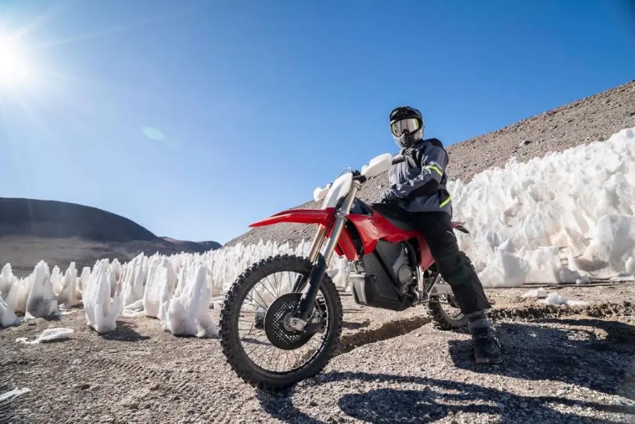 En primer plano una moto eléctrica Stark Varg EX roja a pleno sol pero rodeada de montículos de nieve