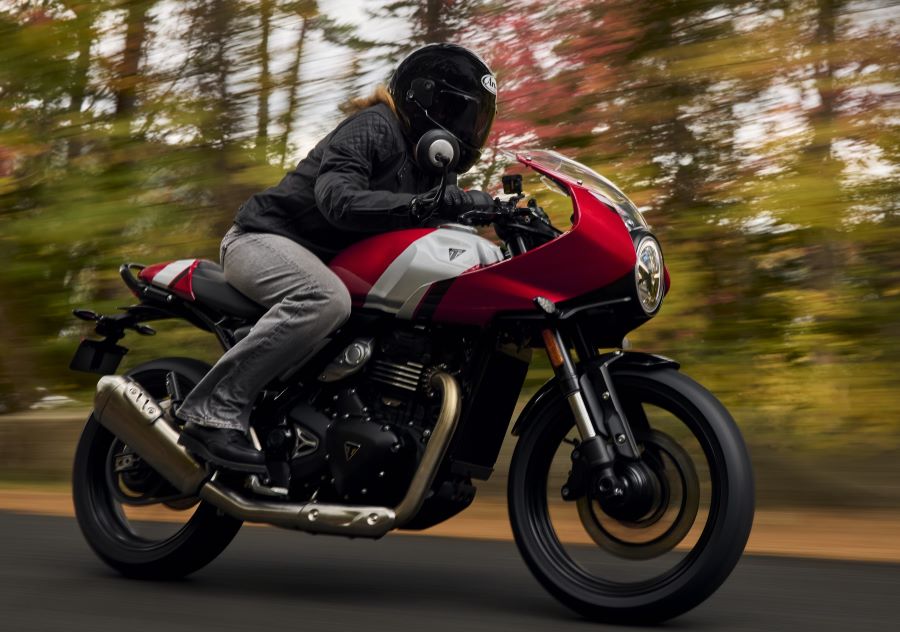 Por qué las Tracker 400 y Thruxton 400 son clave para Triumph Una moto Triumph Thruxton 400 roja circula por una ruta con bosque verde de fondo