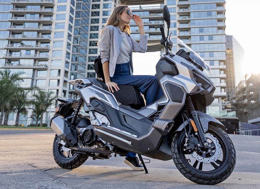 Una mujer sentada de costado sobre un scooter Zanella Cruiser 200 ADV GT con fonde de edificios