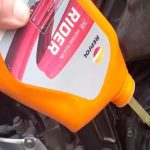 Una mano vierte aceite para moto marca Repsol desde un envase naranja al depósito del vehículo