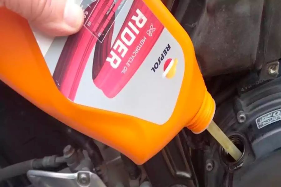 Una mano vierte aceite para moto marca Repsol desde un envase naranja al depósito del vehículo