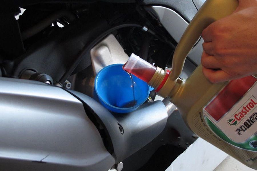 Un usuario vierte el aceite de moto Castrol de un bidón al embudo que conecta con el tanque del vehículo