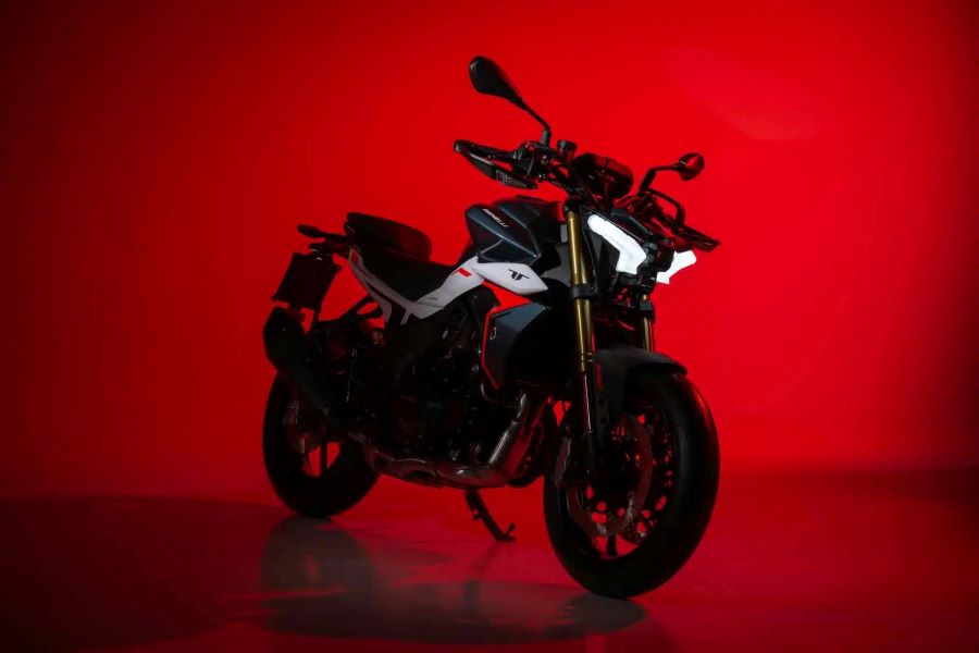 Una moto Benelli TNT 550 azul y blanca con las luces encendidas dispuesta sobre fondo rojo