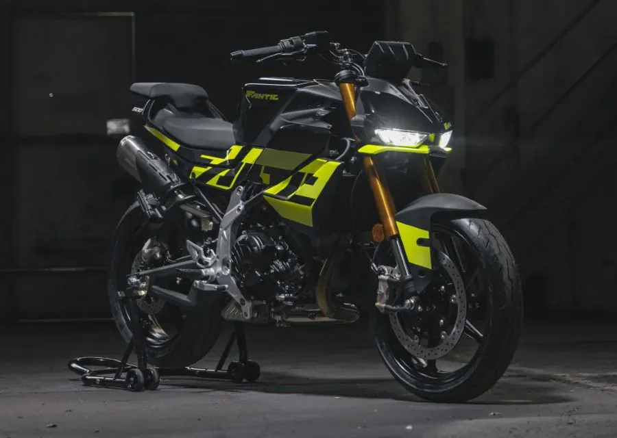 Una moto Fantic Stealth 500 verde fluor y negra con las luces encendidas dentro de un ámbito oscuro