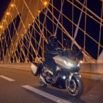 Honda Forza 750: el scooter que piensa como moto grande Un scooter Honda Forza 750 de desplaza de noche, con la luces encendidas, sobre un puente carretero