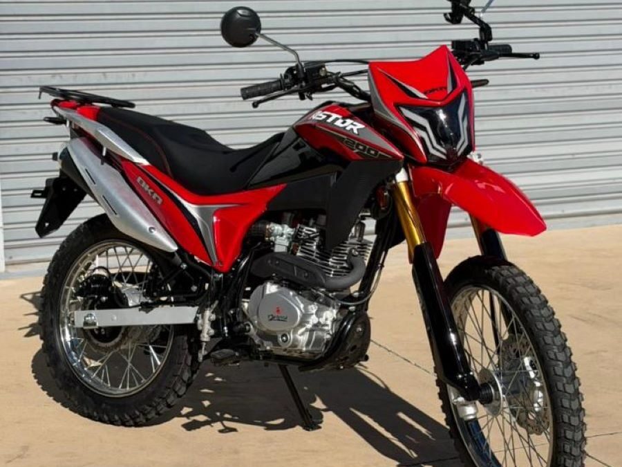 Perfil izquierdo de una moto Okinoi Astor 200 roja a pleno sol y con fondo de una persiana gris