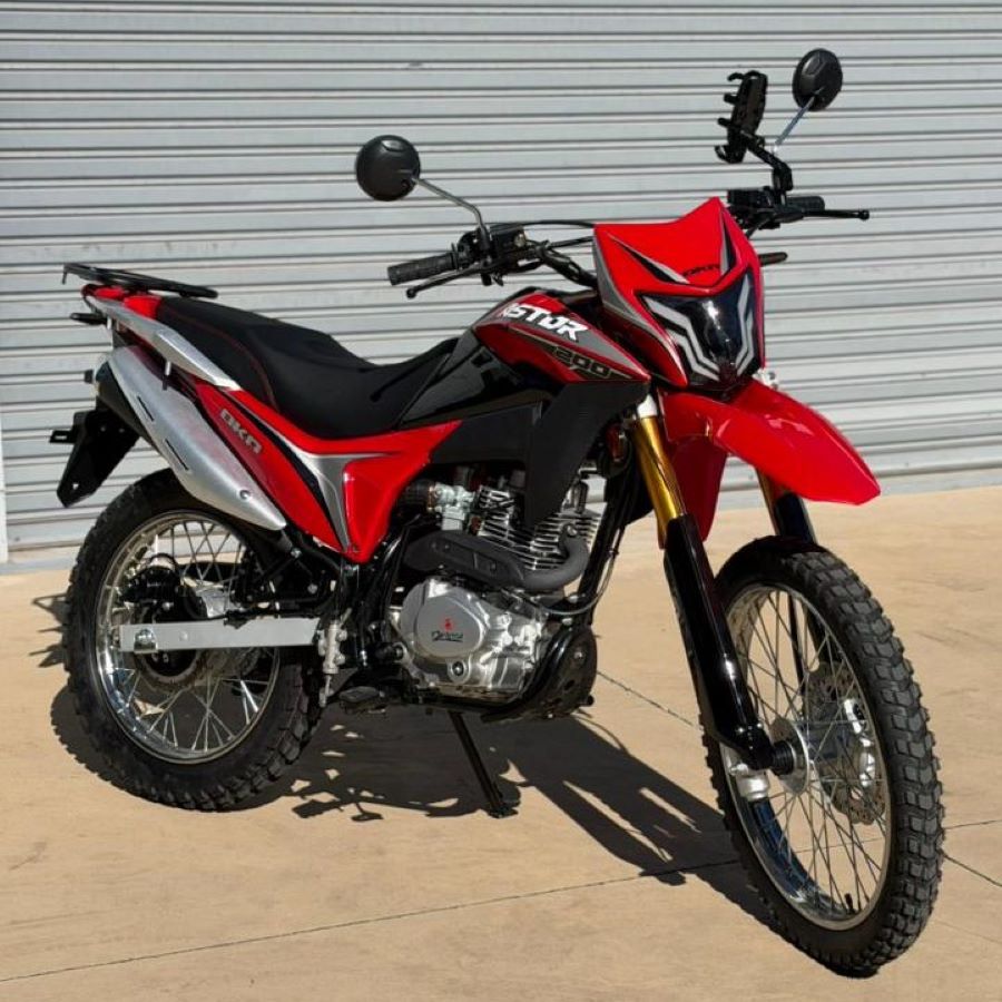 Perfil izquierdo de una moto Okinoi Astor 200 roja a pleno sol y con fondo de una persiana gris