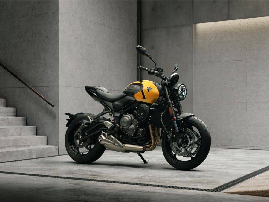 La Trident 660 crece: más motor, chasis y tecnología avanzada Una moto Triumph Trident 660 amarilla posa en una habitación con escalera.