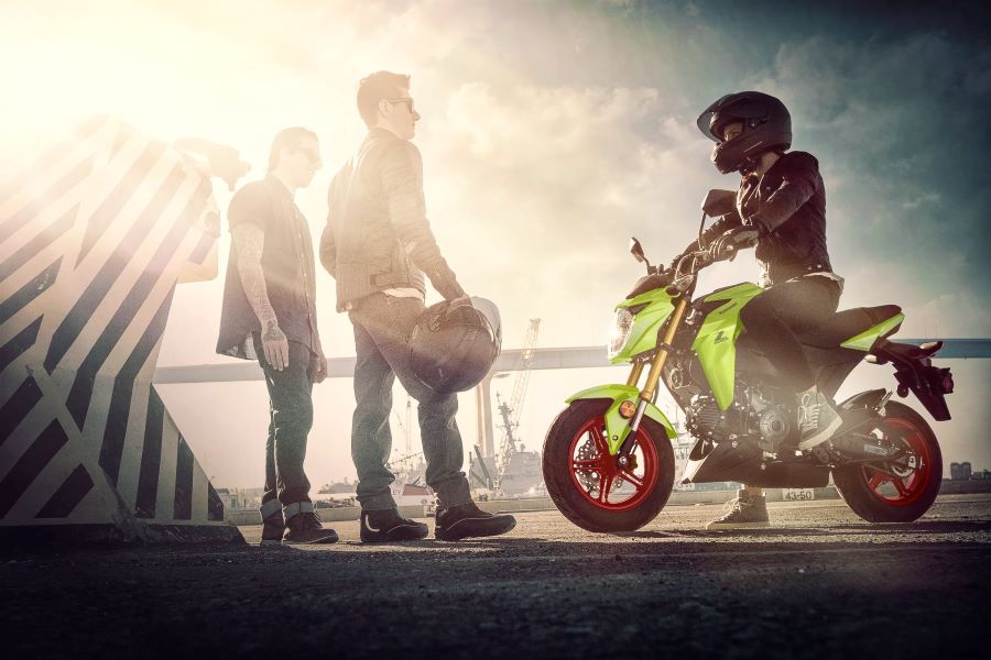 Kawasaki Z125 PRO, la mini Z que se maneja con el ego adelante Un joven dialoga con otros dos sentado sobre una moto Kawasaki Z125 Pro verde