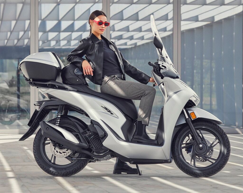 Una bella modelo juvenil posa sobre un scooter Honda SH125i 2026 color claro