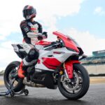 Un piloto, con casco colocado, se acomoda los guantes sentado sobre una moto Yamaha R9 70 Aniversario