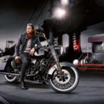 Un modelo posa sobre una moto custom calzada con neumáticos Avon Cobra Chrome de banda blanca