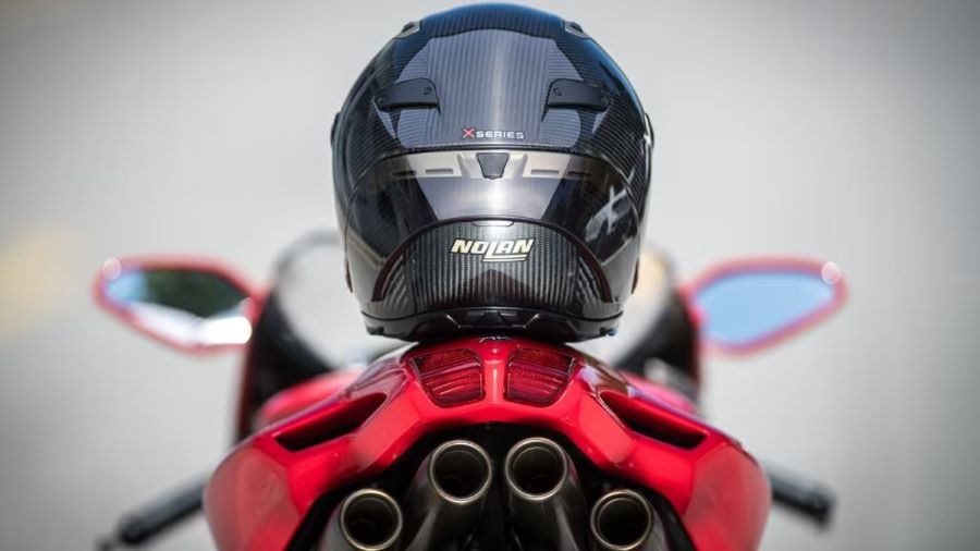 Un casco Nolan X-Series negro posa desde el asiento de una moto deportiva roja