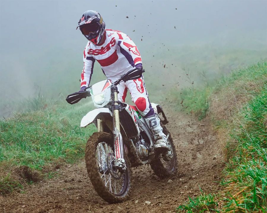 Un piloto, parados sobre los pedalines, avanza en el barro con una moto Bimota BX450