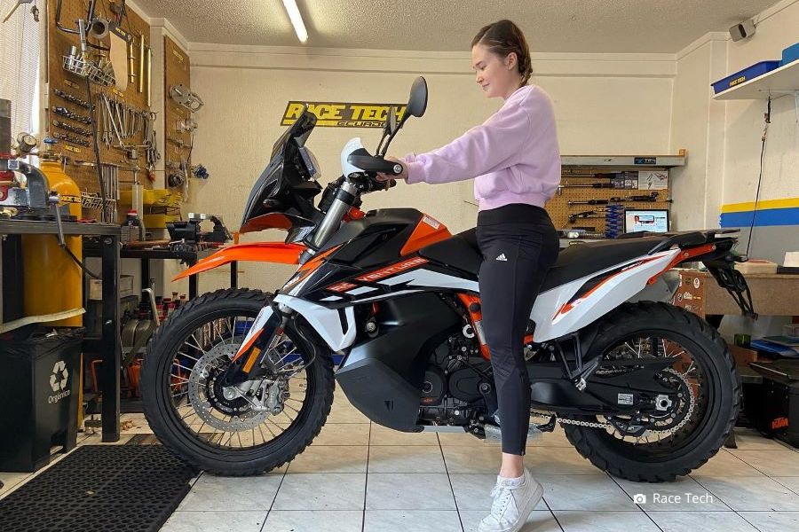 Una señorita sentada en su moto, que apenas toca el piso con las puntas de los pies, mira el tablero