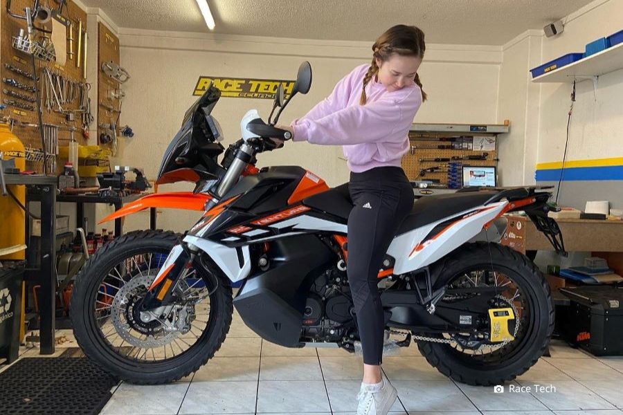 Una señorita, que apenas toca el piso con las puntas de los pies, mira hacia abajo de su moto
