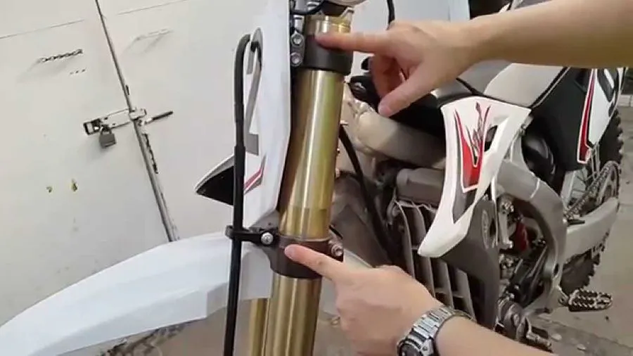 Dos manos señalan una horquilla delantera de una moto