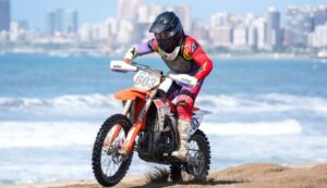 Un pìloto de competición surca la arena con el mar y una ciudad de fondo